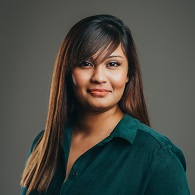 Person smiling wearing a green blouse against a gray background.